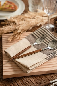 Macro detail of stainless steel cutlery with brown handles on linen napkin and wood tray