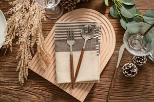 Flat lay of stainless steel cutlery with wood handles on a striped cotton napkin