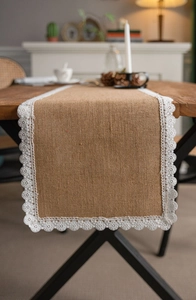Detail of natural jute table runner featuring white floral lace embroidery on wooden table