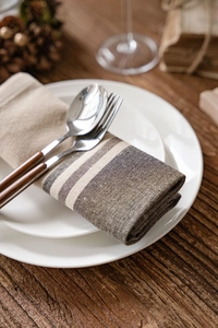 Detail of striped linen napkin with wooden cutlery set on ceramic plates for rustic dining