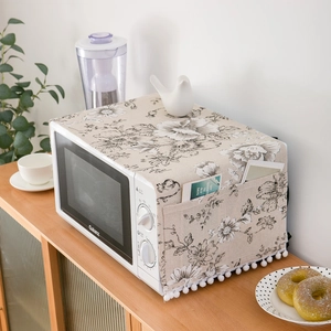 Detail of linen microwave dust cover with black floral pattern and white tassel fringe