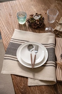 Top-down detail of linen coffee-striped placemat with ceramic plates on wood table
