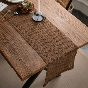 Handwoven khaki table runner with hollow crochet texture and fringe on wood table