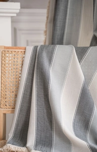 Detail of striped yarn-dyed fabric with cream tassels on a rustic chair background