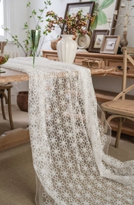 Detailed view of white floral lace table runner on a rustic wooden dining table