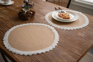 Detail of round burlap placemat with white floral lace trim on dark wood dining table