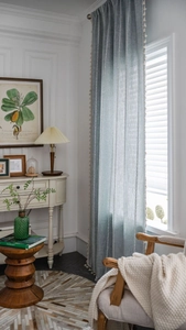 Détail du rideau en lin bleu-gris avec broderie blanche et pompons beiges sur le côté