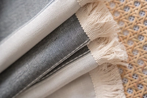 Detail of striped cotton linen curtain fabric with cream fringes on a rattan tray