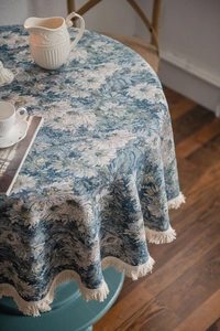 Detail of blue floral jacquard round tablecloth with decorative fringe tassels on edges