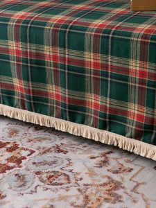 Close-up of vintage green and red plaid blanket fabric with dense cream tassels