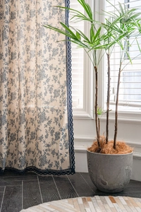 Detail of blue floral cotton linen curtain with navy lace trim in cozy interior setting