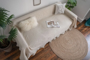 Detail of beige cotton linen sofa cover with elegant ruffle edge on a wooden floor