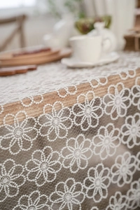 Close-up of white floral lace tablecloth with intricate daisy hollow pattern on wood table
