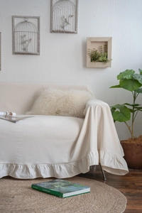 Detail of elegant cream white sofa cover featuring a ruffled hem in a cozy living room