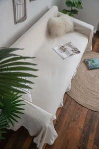 Close-up of ruffled edges on a cream white fabric sofa cover in a cozy living room