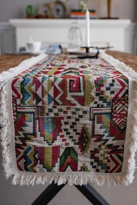 Detail of colorful geometric jacquard table runner with decorative off-white tassels