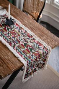 Close-up of geometric jacquard table runner with tassels on a rustic wooden table