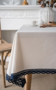 Detailed close-up of cream cotton linen tablecloth featuring dark blue hollow lace trim