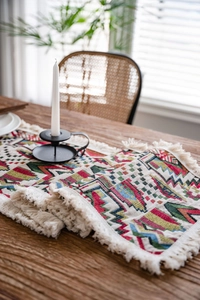 Detail of colorful geometric woven table runner with white tassels on dark wood table