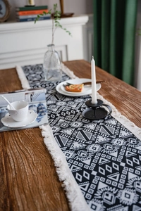 Detail of black and white geometric table runner with tassels on a rustic wooden table