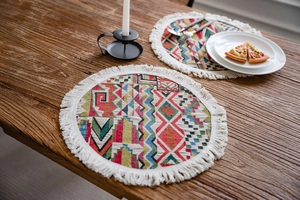 Detail of colorful geometric woven table mat with white cotton tassels on wood table