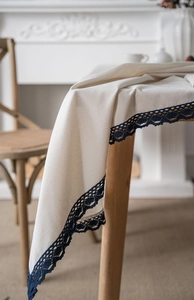 Close-up of beige linen tablecloth featuring intricate dark blue hollow lace trim detail