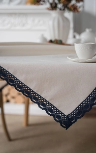 Close-up of cream linen tablecloth featuring intricate navy blue lace edge detailing