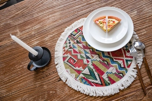 Detail of colorful geometric bohemian woven placemat with white fringe on a wooden table