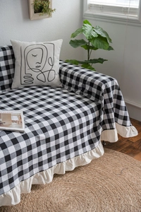 Detailed close-up of black and white checkered sofa cover with cream ruffle lace edges