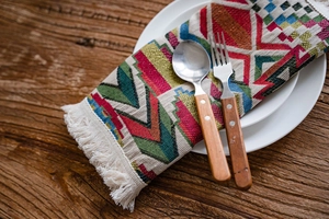 Close-up of geometric jacquard table runner with fringe on a rustic wooden dining table