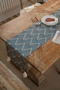 Detail of dark blue geometric pattern table runner with beige tassels on a wooden dining table