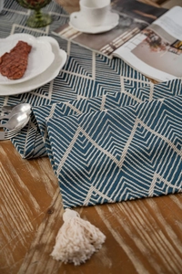 Detail of blue and white geometric table runner with white tassels on a wooden surface
