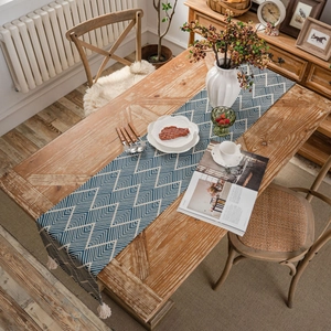 Navy blue geometric diamond table runner with cream tassels on rustic wooden table