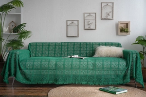 Detail of emerald green crochet sofa cover with hollow geometric patterns and long fringes