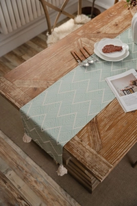 Detail of Nordic green geometric herringbone table runner with handmade tassels on wood
