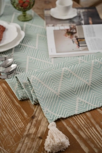 Close-up of green geometric jacquard table runner with cotton fringe on wooden surface