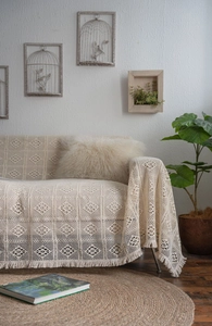 Close-up of beige crochet sofa throw blanket with geometric patterns and fringe detail