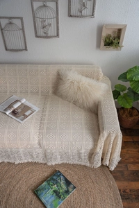 Detailed close-up of beige crochet sofa throw with geometric cutouts and dense fringe trim