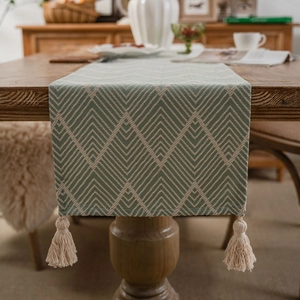 Green and beige geometric jacquard table runner with tassels on a wooden dining table