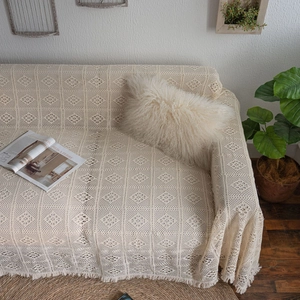 Beige hollow crochet sofa cover with fringe edges in a cozy rustic home setting