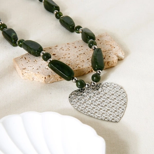 Detail of green beaded necklace featuring a large hammered silver heart pendant on stone