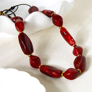 Retro necklace with dark red acrylic beads and gold-plated hematite spacers on white ceramic