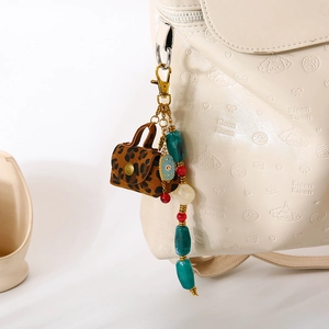 Porte-clés œil maléfique plaqué or avec mini sac léopard sur un sac à dos beige