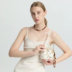 Detail of cream quilted mini bag with golden chain and colorful beaded stone charm