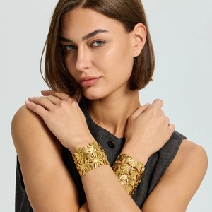 Detail of 18K gold-plated stainless steel cuff bracelets with daisy and ginkgo leaf cutouts