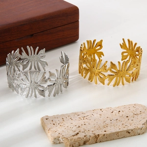 Detailed macro view of 18K gold and silver ginkgo leaf open cuffs on natural stone and wood
