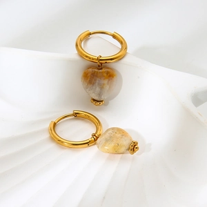 Detailed close-up of golden heart-shaped natural stone earrings on a white shell prop