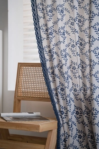 Close-up of beige linen curtain with blue floral prints and intricate lace edge trim