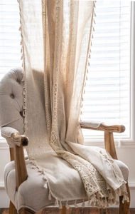 Detail of beige linen curtains featuring bohemian hollow lace crochet and fringe tassels