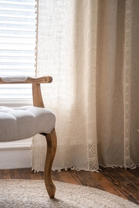 Detail of beige linen curtain featuring decorative tassels and crochet lace embroidery